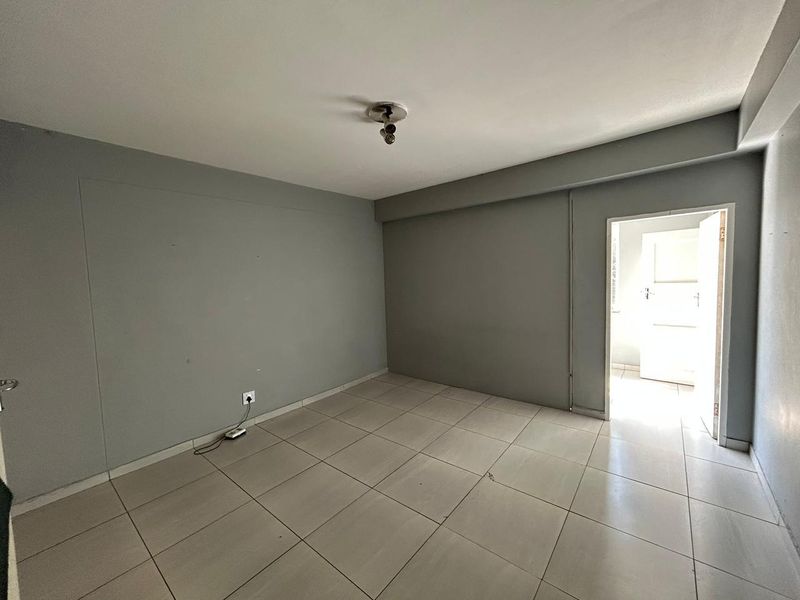 An empty bedroom featuring neutral grey walls and light-colored floor tiles, providing a blank canvas for personalization.