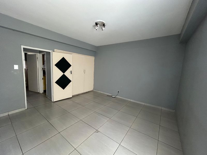 An empty bedroom featuring tiled flooring, built-in cupboards, and neutral grey walls, offering a blank canvas for personalization.