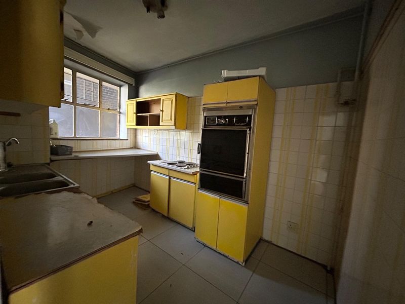A dated kitchen featuring original yellow cabinetry, built-in oven, electric hob, and tiled splashbacks, requiring significant renovation to modernize the space.