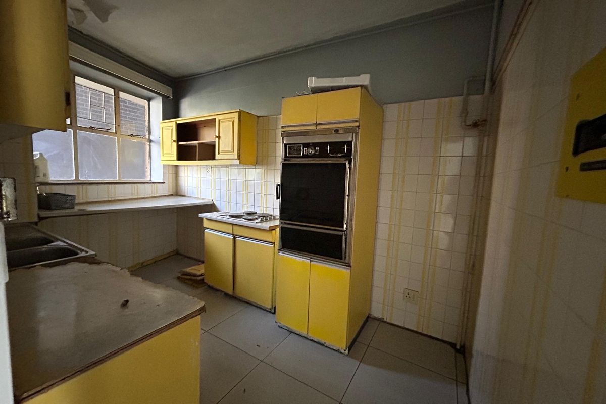 A dated kitchen featuring original yellow cabinetry, built-in oven, cooktop, and tiled splashbacks, requiring significant renovation to modernize the space.