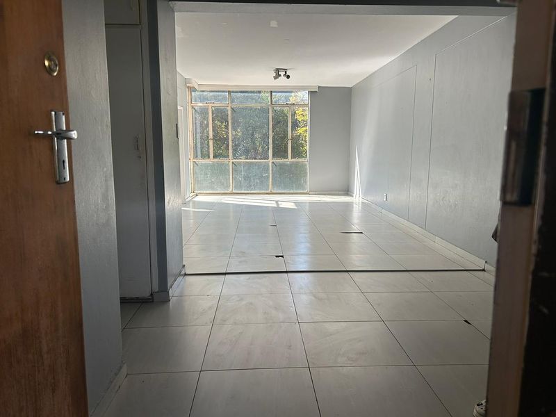 An empty, open-plan living area featuring large windows and tiled flooring, requiring some maintenance to the floor finishes.