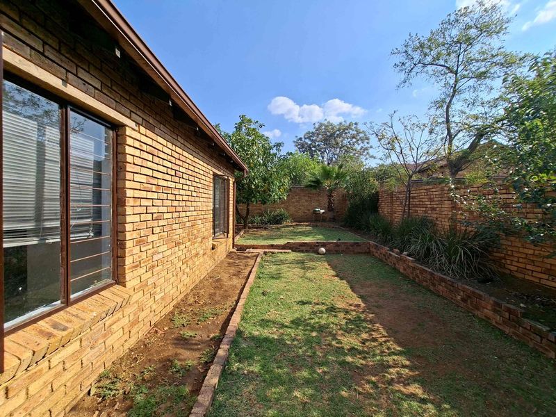 A private rear garden featuring face brick boundary walls, terraced lawn areas, and established trees, providing a low-maintenance outdoor space.