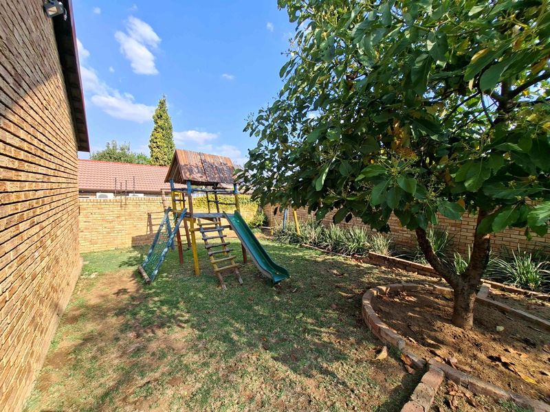 A private rear garden featuring a brick boundary wall, mature tree with a brick planter, and a grassy area with a children's play structure.