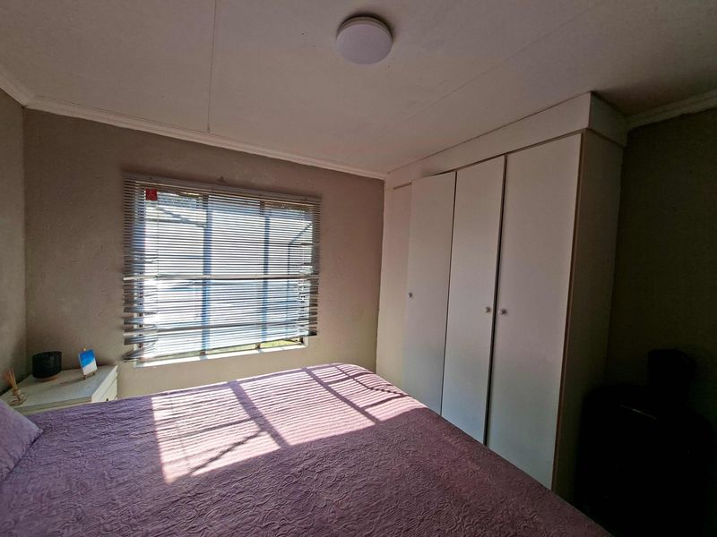 A functional bedroom featuring a built-in wardrobe, venetian blinds, and a ceiling light fixture, offering a neutral base for personalization.