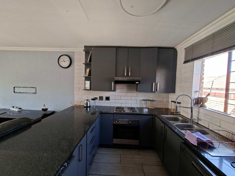 A functional kitchen featuring dark cabinetry, granite countertops, a built-in oven with hob, and a double basin sink with a modern mixer tap.