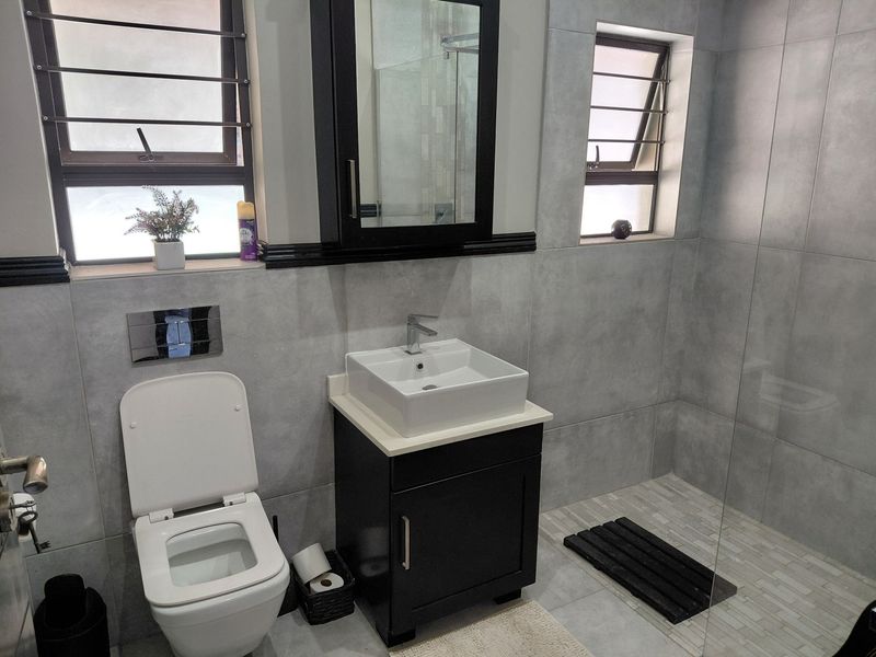 Modern bathroom featuring a wall-mounted toilet, vanity with vessel sink, and a glass-enclosed shower with contemporary grey tiling.