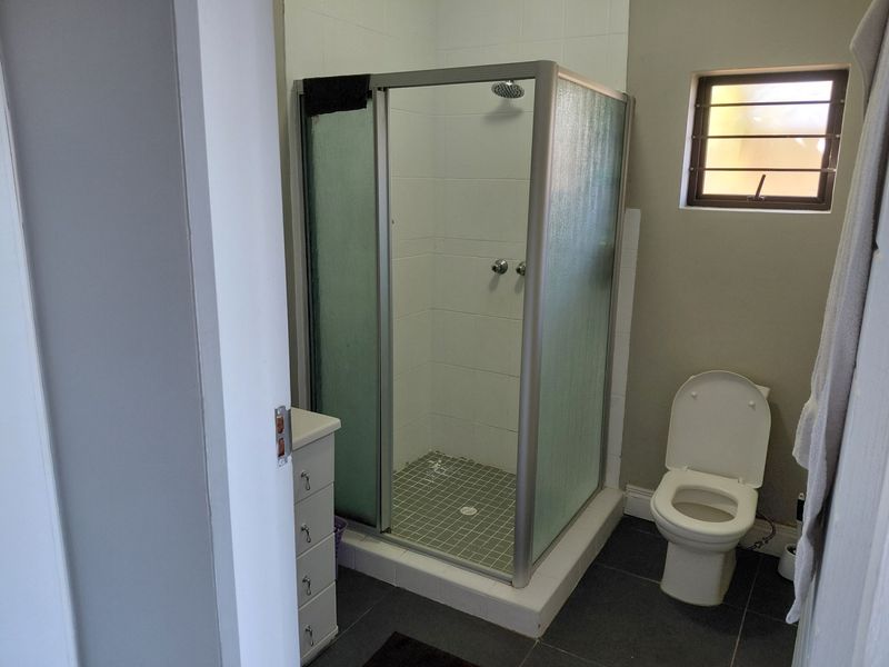 A functional bathroom featuring a corner shower enclosure, toilet, and built-in vanity with tiled flooring and walls.