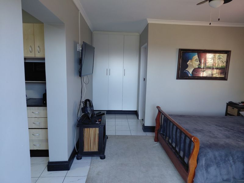 Spacious bedroom featuring built-in cupboards, tiled flooring, and a ceiling fan, with an adjacent alcove area.