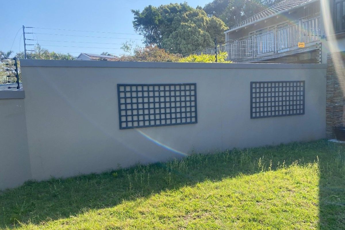 A well-maintained perimeter boundary wall featuring integrated electric fencing and decorative trellis panels, set against a grassed garden area.
