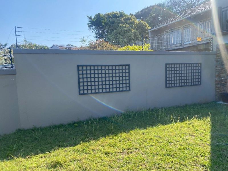 A well-maintained perimeter boundary wall featuring integrated electric fencing and decorative trellis panels, set against a grassed garden area.