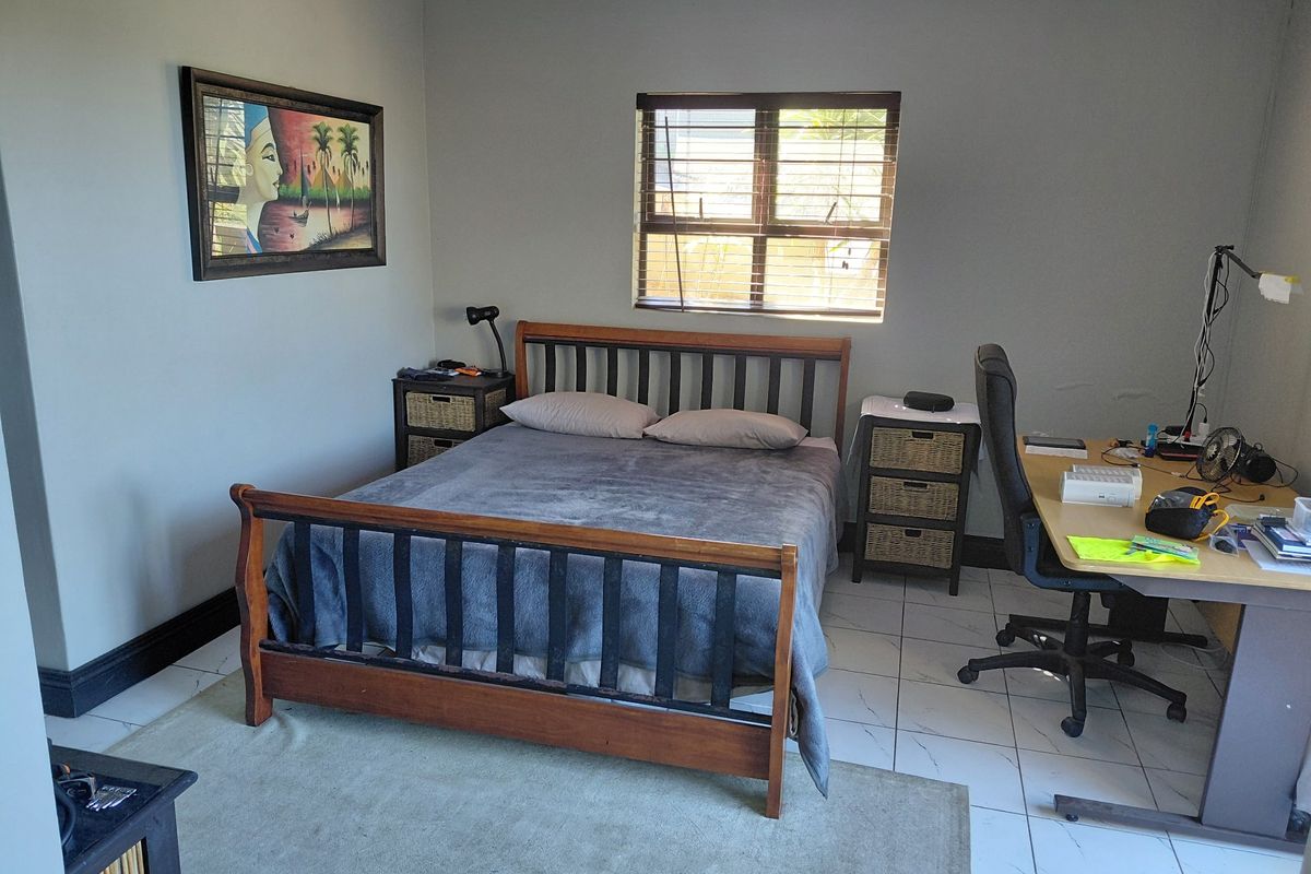 A functional bedroom featuring tiled flooring, neutral wall paint, and a window with fitted blinds.