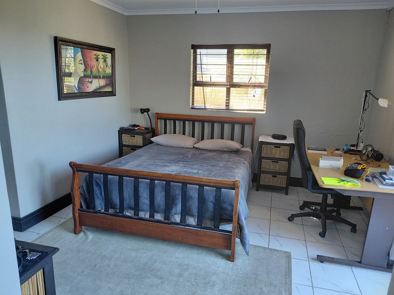 A functional bedroom featuring tiled flooring, neutral wall paint, and a window with fitted blinds.