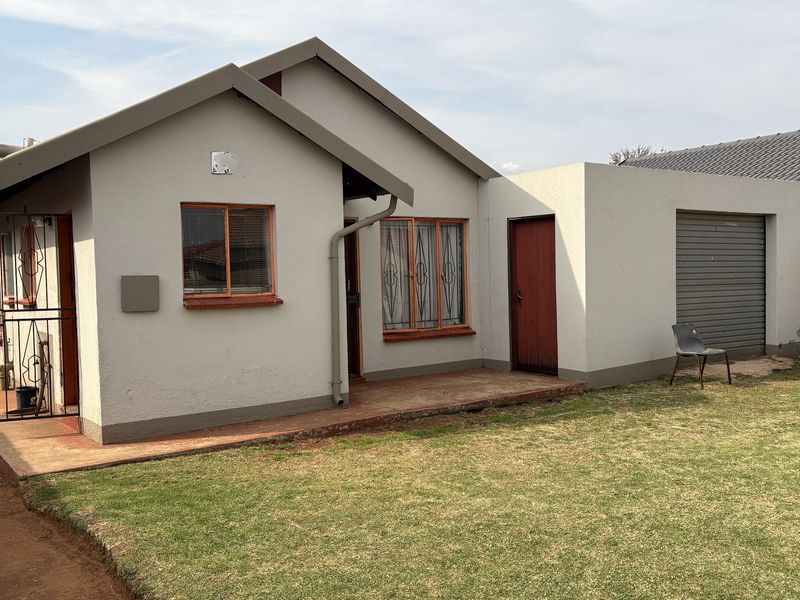 Rear view of the house featuring a small patio, attached garage with a roller door, and security gates on windows and doors.