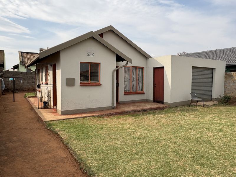 Rear view of the house featuring a small lawn, concrete patio, and an attached garage with a roller door.