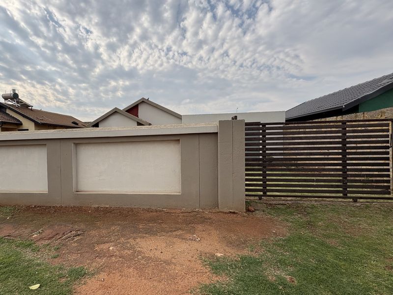 Front exterior view featuring a solid perimeter wall with a horizontal slatted metal gate and a solar water heater visible on the roof.