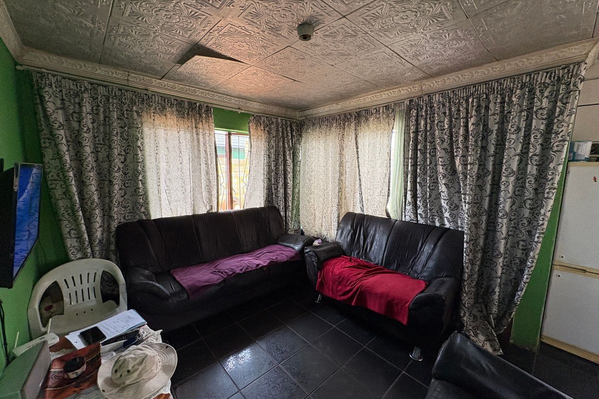 Living room featuring dark tiled flooring and decorative ceiling tiles, requiring cosmetic updates to improve the overall aesthetic and condition of the space.