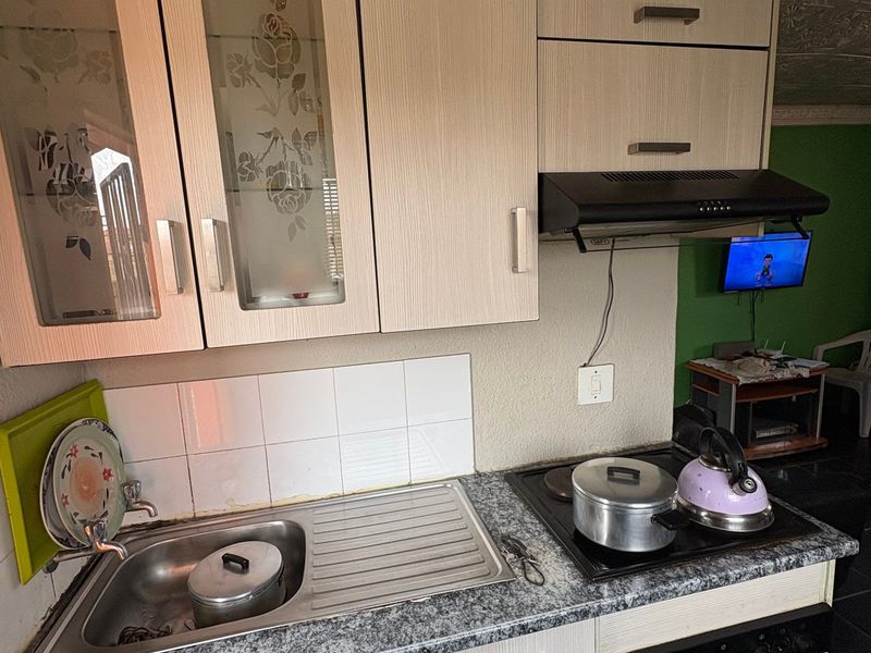 Compact kitchen featuring light wood-grain cabinetry, a stainless steel sink, built-in oven, electric hob, and extractor fan with a tiled backsplash.