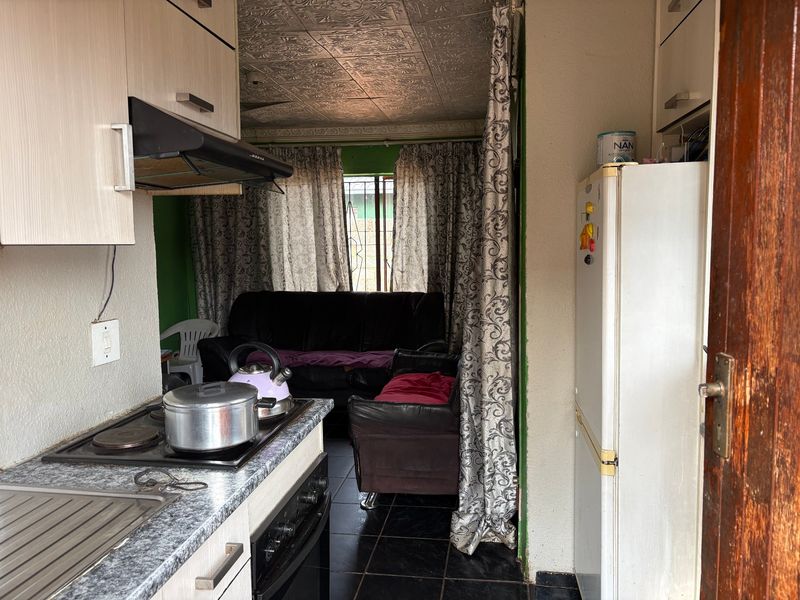 Compact open-plan kitchen and living area featuring built-in cabinetry, electric hob, extractor fan, and decorative ceiling tiles.