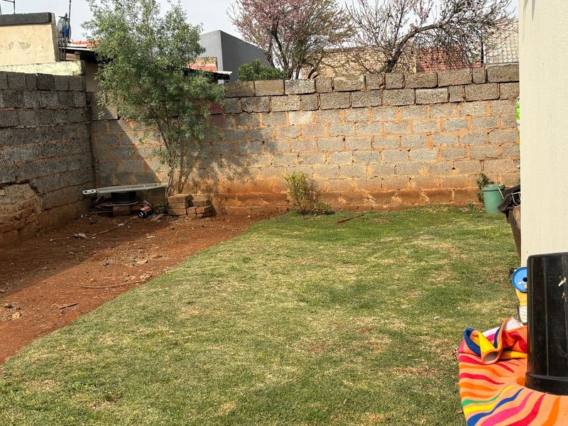 A private rear garden area featuring a lawn and a cinder block boundary wall, offering potential for landscaping and outdoor improvement.