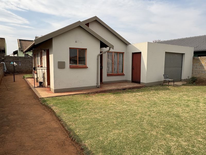 Rear view of a detached house featuring a small lawn, concrete patio, and an attached garage with a roller door.