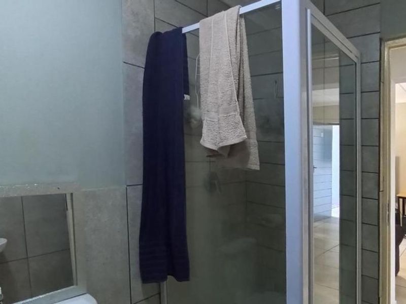A functional bathroom featuring a glass shower enclosure, tiled walls, and floor tiling, with a view into the adjacent living area.