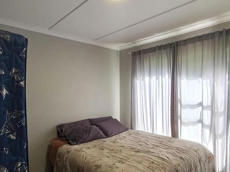A functional bedroom featuring a built-in wardrobe and large windows with curtains, providing natural light and storage space.