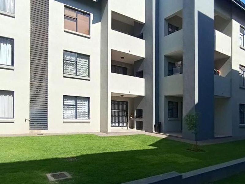 Rear view of a modern apartment complex featuring a communal lawn, private balconies, and built-in braai facilities.