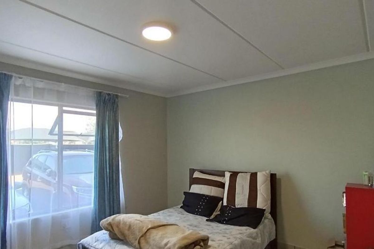 A standard bedroom featuring neutral wall tones, a ceiling panel finish, and a window providing natural light.