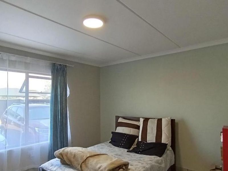 A standard bedroom featuring neutral wall tones, a ceiling panel finish, and a window providing natural light.