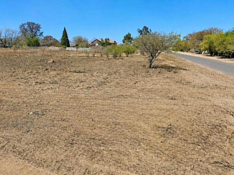 A vacant residential plot of land featuring dry vegetation and direct access to a paved street in a quiet neighborhood setting.