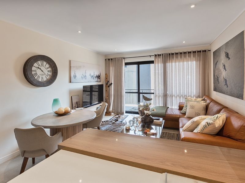An open-plan living and dining area featuring a breakfast bar, recessed lighting, and sliding glass doors leading to a balcony.