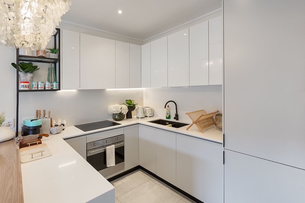 Modern kitchen featuring sleek white cabinetry, quartz countertops, integrated appliances, and high-quality finishes with under-cabinet lighting.
