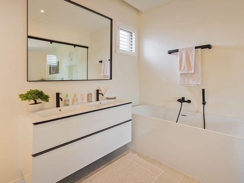 Modern bathroom featuring a sleek double vanity, freestanding bathtub, and contemporary black matte fixtures with a large wall-mounted mirror.
