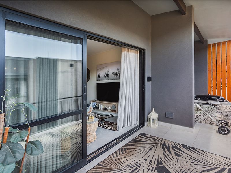 A modern covered balcony featuring large sliding glass doors, tiled flooring, and a timber slat privacy screen, providing a seamless transition to the living area.