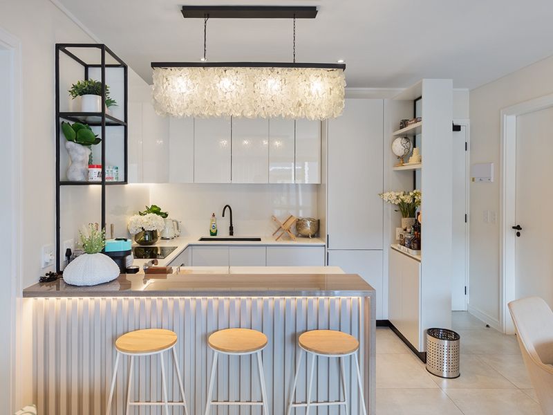 Modern kitchen featuring sleek white cabinetry, stone countertops, integrated appliances, and a stylish breakfast bar with integrated LED lighting.