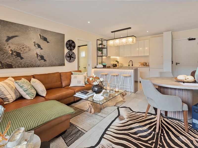 Modern open-plan living area featuring a sleek kitchen with island, contemporary lighting, and neutral tiled flooring, creating a cohesive and functional space.
