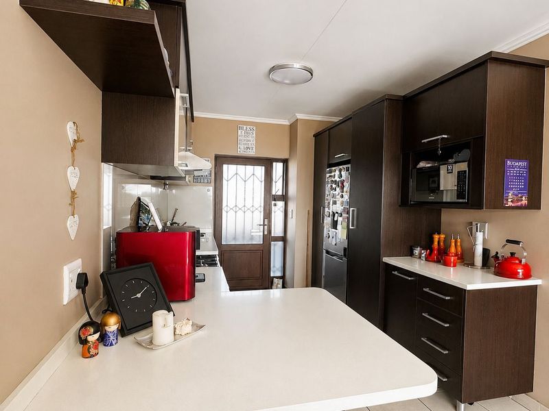 A functional kitchen featuring dark wood cabinetry, white countertops, tiled flooring, and integrated appliances, leading to an exterior door.