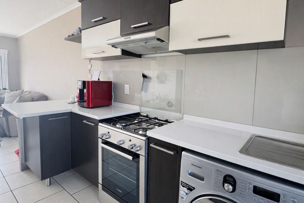 Modern kitchen featuring dark and white cabinetry, stone countertops, a gas stove with extractor, and a built-in washing machine.