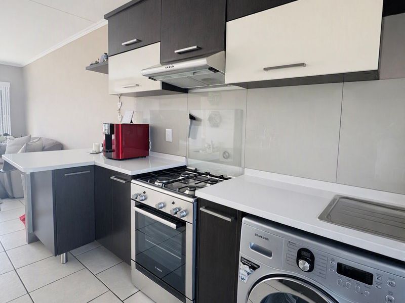 Modern kitchen featuring dark and white cabinetry, stone countertops, a gas stove with extractor, and a built-in washing machine.
