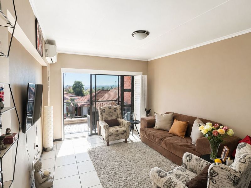 A bright living room featuring tiled flooring, a wall-mounted air conditioning unit, and sliding glass doors that open onto a balcony.