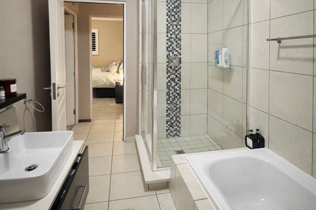 Modern bathroom featuring a glass-enclosed shower, a separate bathtub, and a contemporary vessel sink vanity with neutral wall and floor tiling.