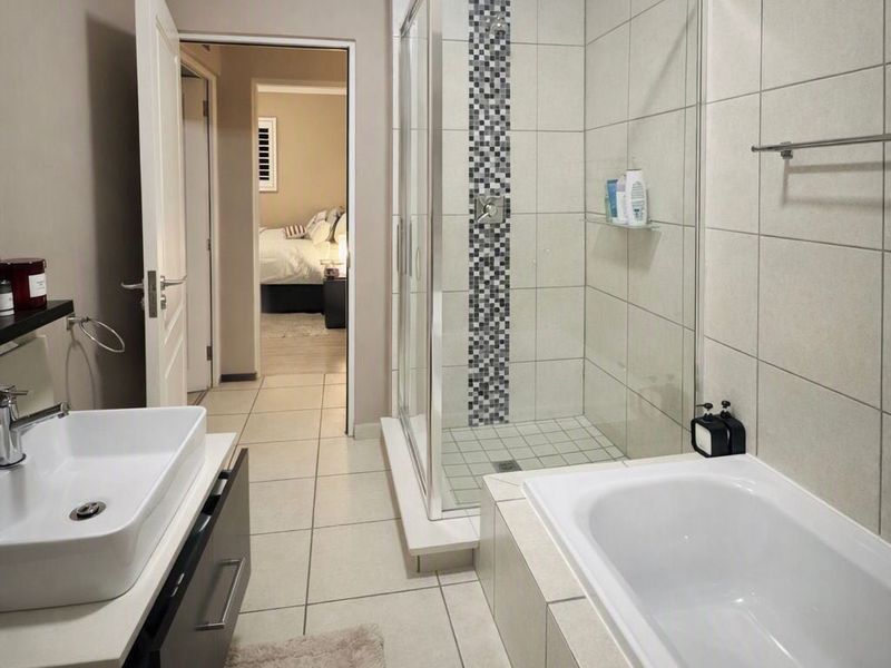 Modern bathroom featuring a glass-enclosed shower, a separate bathtub, and a contemporary vessel sink vanity with neutral wall and floor tiling.