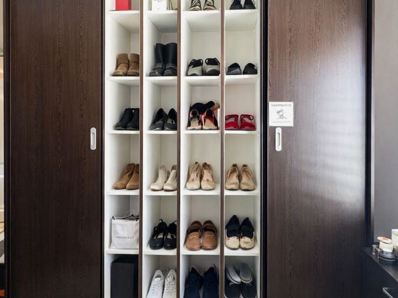 A well-maintained built-in wardrobe featuring dark wood sliding doors and organized vertical shelving units for storage.