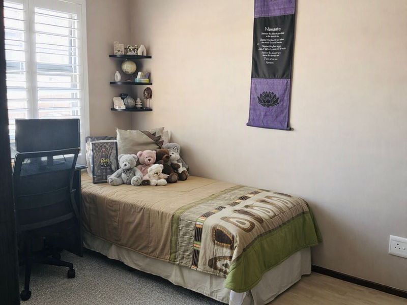 A compact bedroom featuring light laminate flooring, neutral wall tones, and white plantation shutters, providing a clean and functional living space.