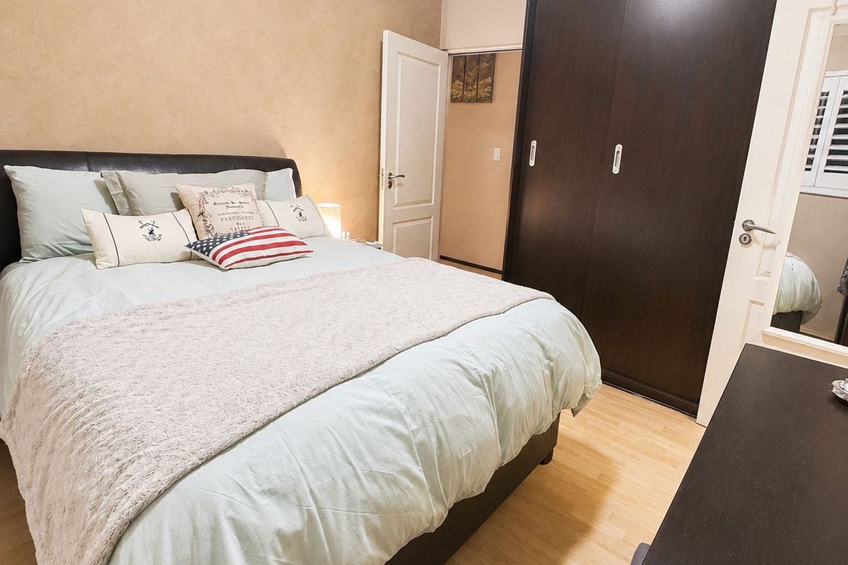 A well-maintained bedroom featuring laminate flooring, neutral wall finishes, and a large dark-toned built-in wardrobe with sliding doors.