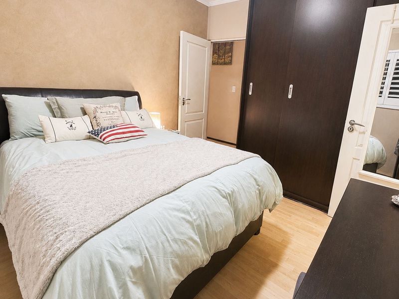 A well-maintained bedroom featuring laminate flooring, neutral wall finishes, and a large dark-toned built-in wardrobe with sliding doors.