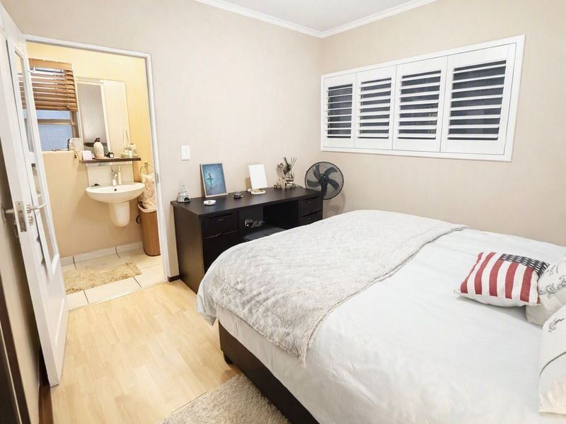 A well-maintained bedroom featuring laminate flooring, plantation shutters, and an adjoining en-suite bathroom with a pedestal basin.
