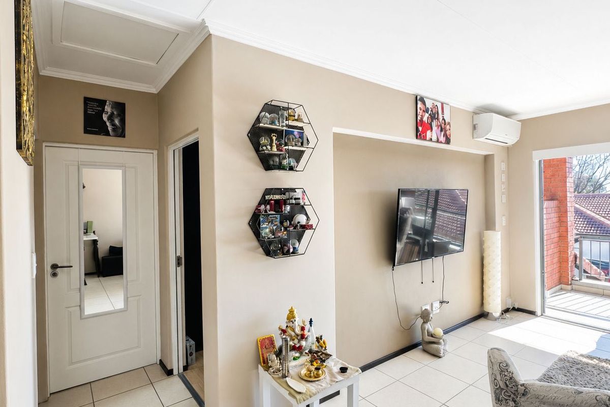A bright living room featuring tiled flooring, a wall-mounted air conditioning unit, and a sliding glass door leading to an outdoor balcony.