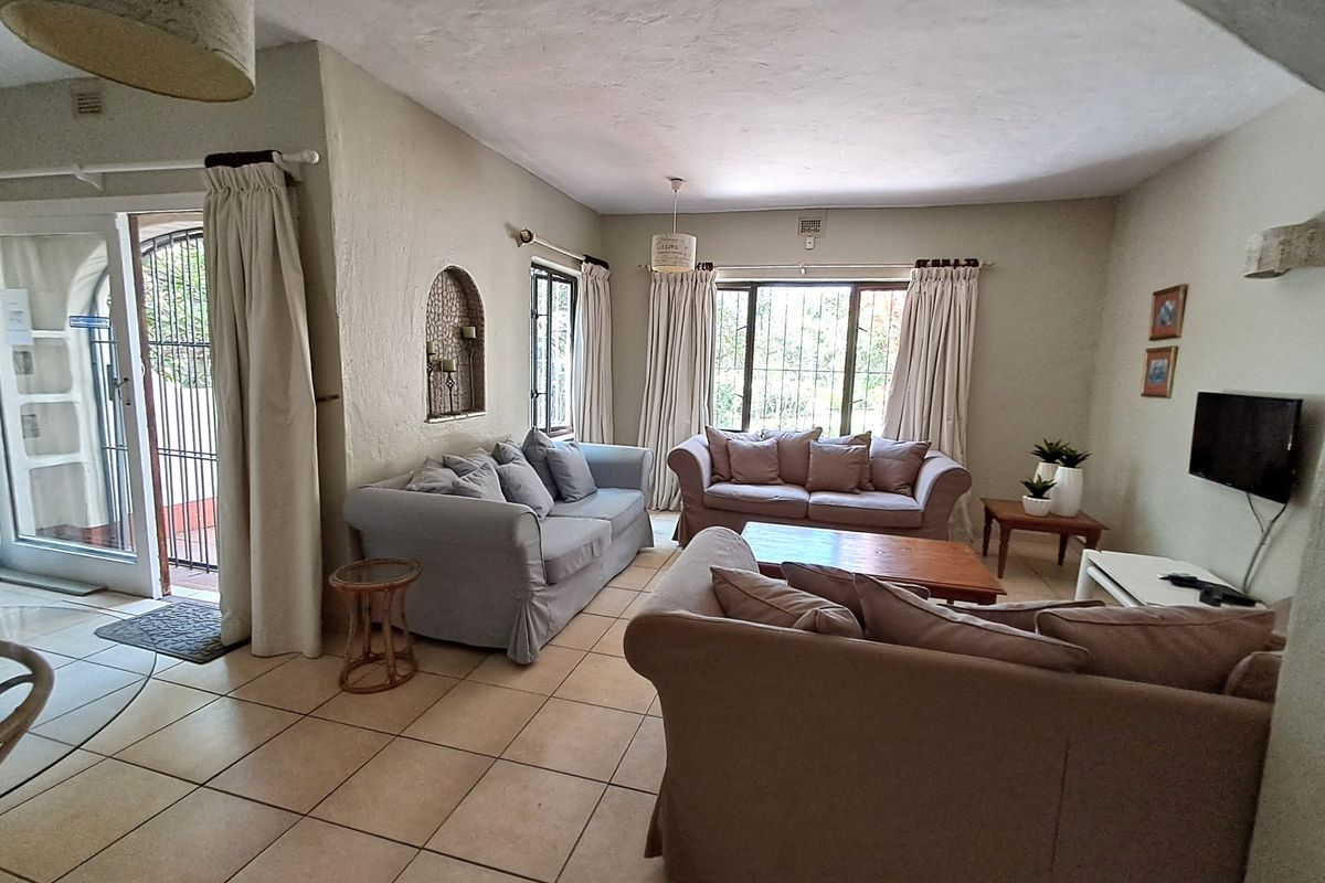 A comfortable living room featuring tiled flooring, an arched wall niche, and large windows with security bars, providing access to the exterior.