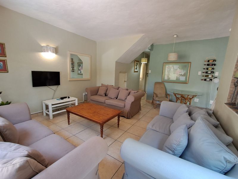 A comfortable living room featuring tiled flooring, wall-mounted lighting, and a sloped ceiling, providing a functional and inviting space for relaxation.